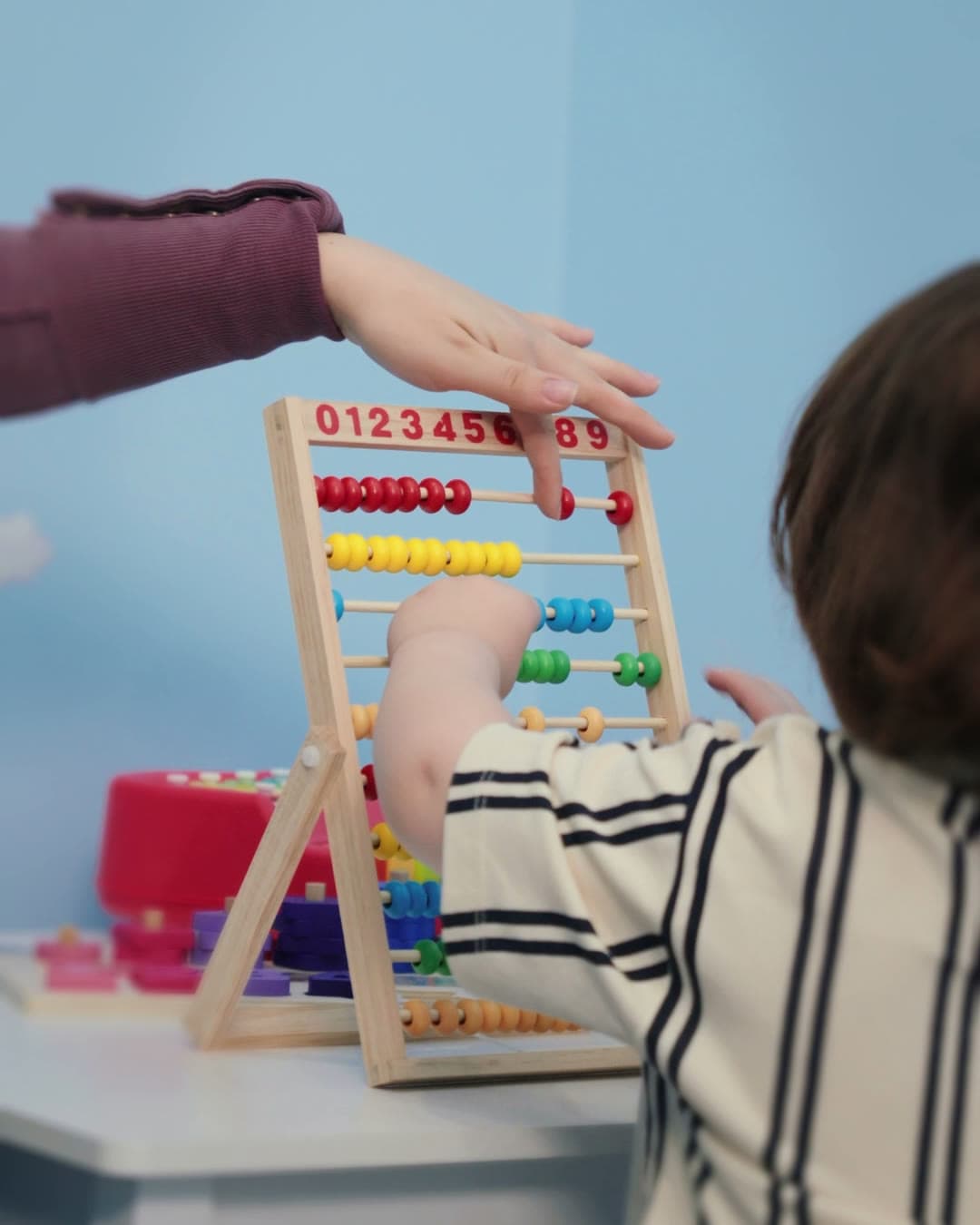 A child counting beads on a wooden abacus with a therapist's help