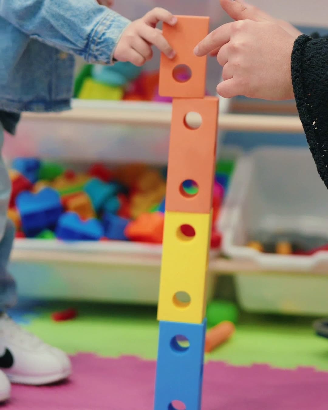 A child and a therapist stacking colorful blocks together