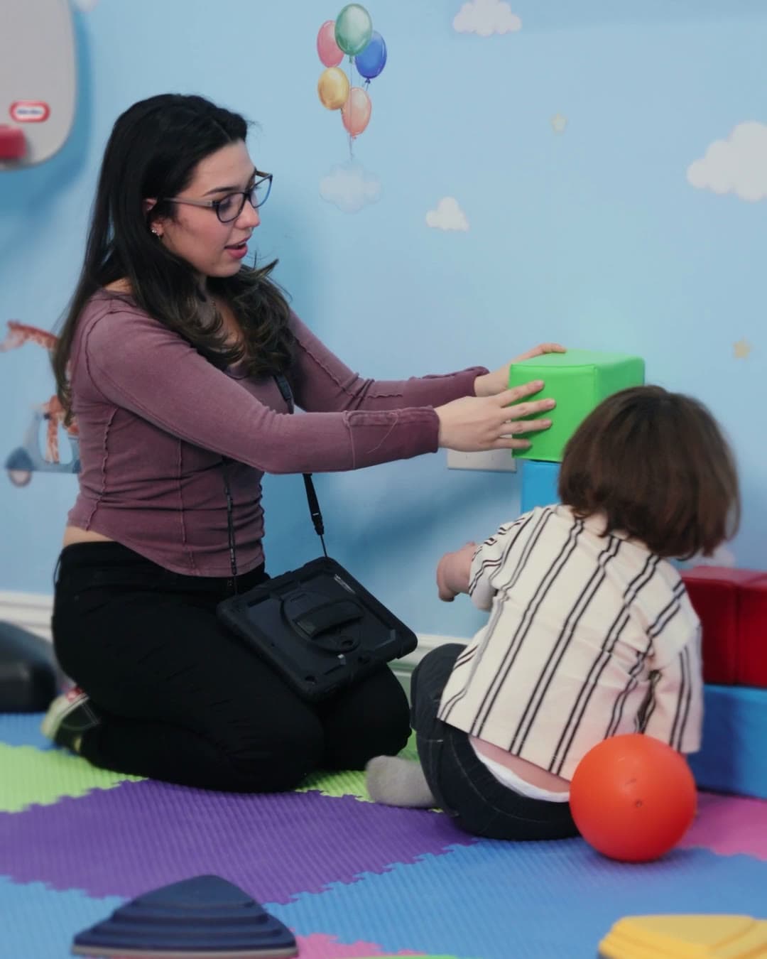 A Sunny therapist and a child building with foam blocks on the play mats