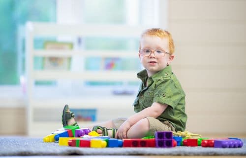 Child playing on the floor A child with glasses sitting on the floor among colorful building blocks