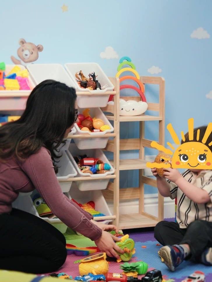 A Sunny therapist and a child playing with toys on the playroom floor
